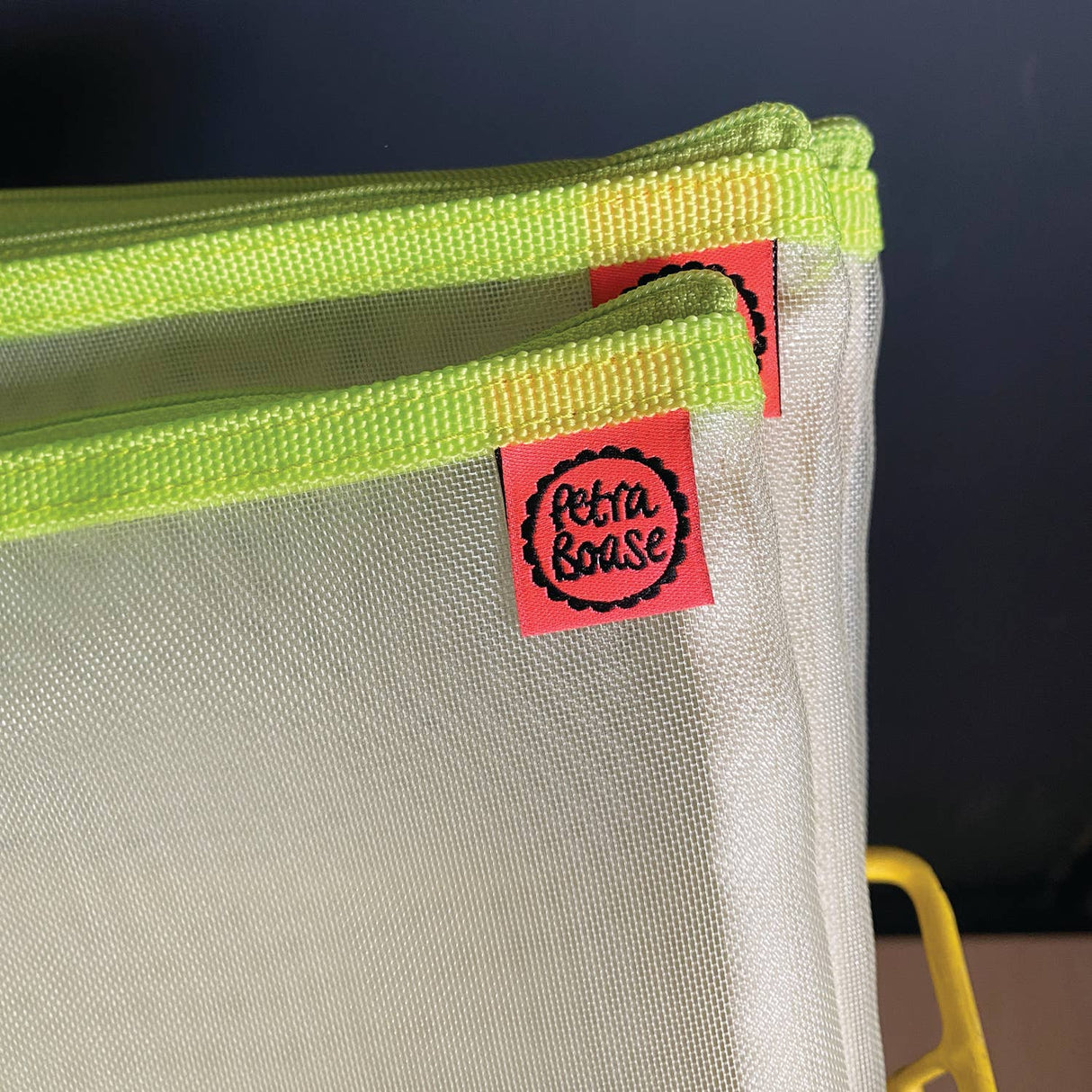 Close-up of an acid yellow and beige bag with a red label featuring 'Petra Boase' branding.