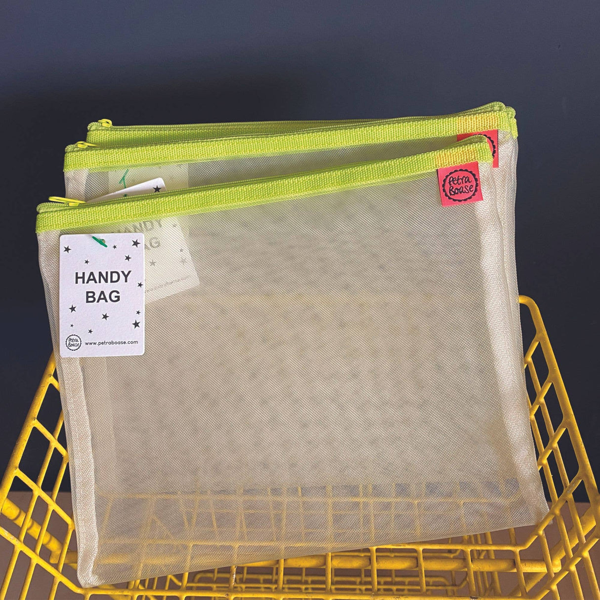 Mesh handy bag with green zipper on a yellow metal basket against a dark background