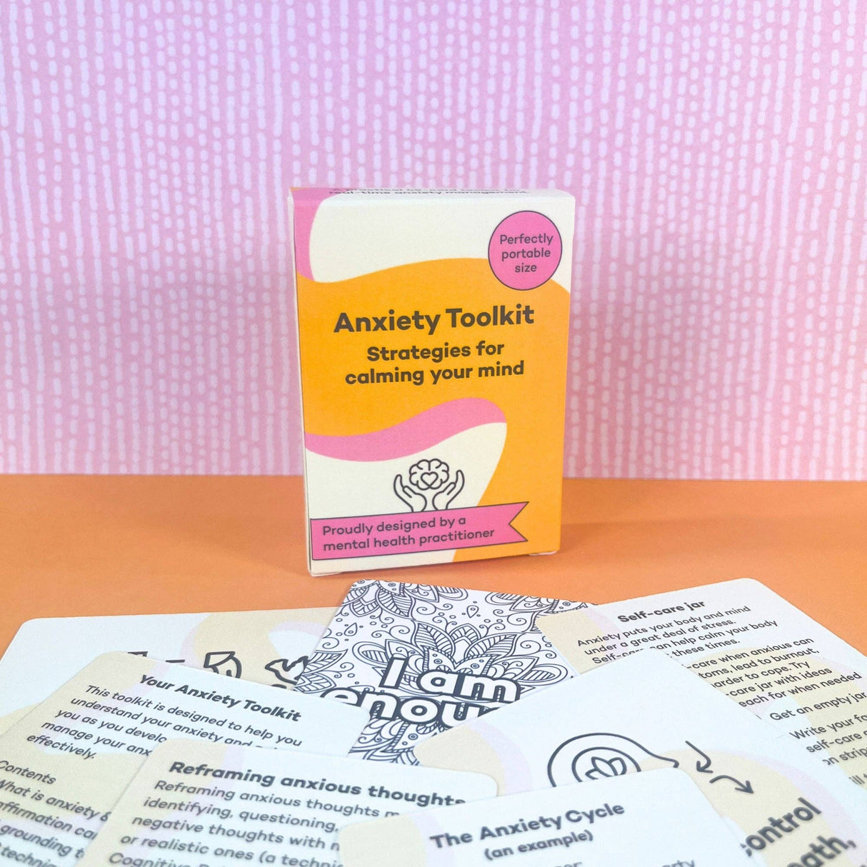 Anxiety Toolkit box displayed upright on an orange surface surrounded by fanned-out cards showing card content