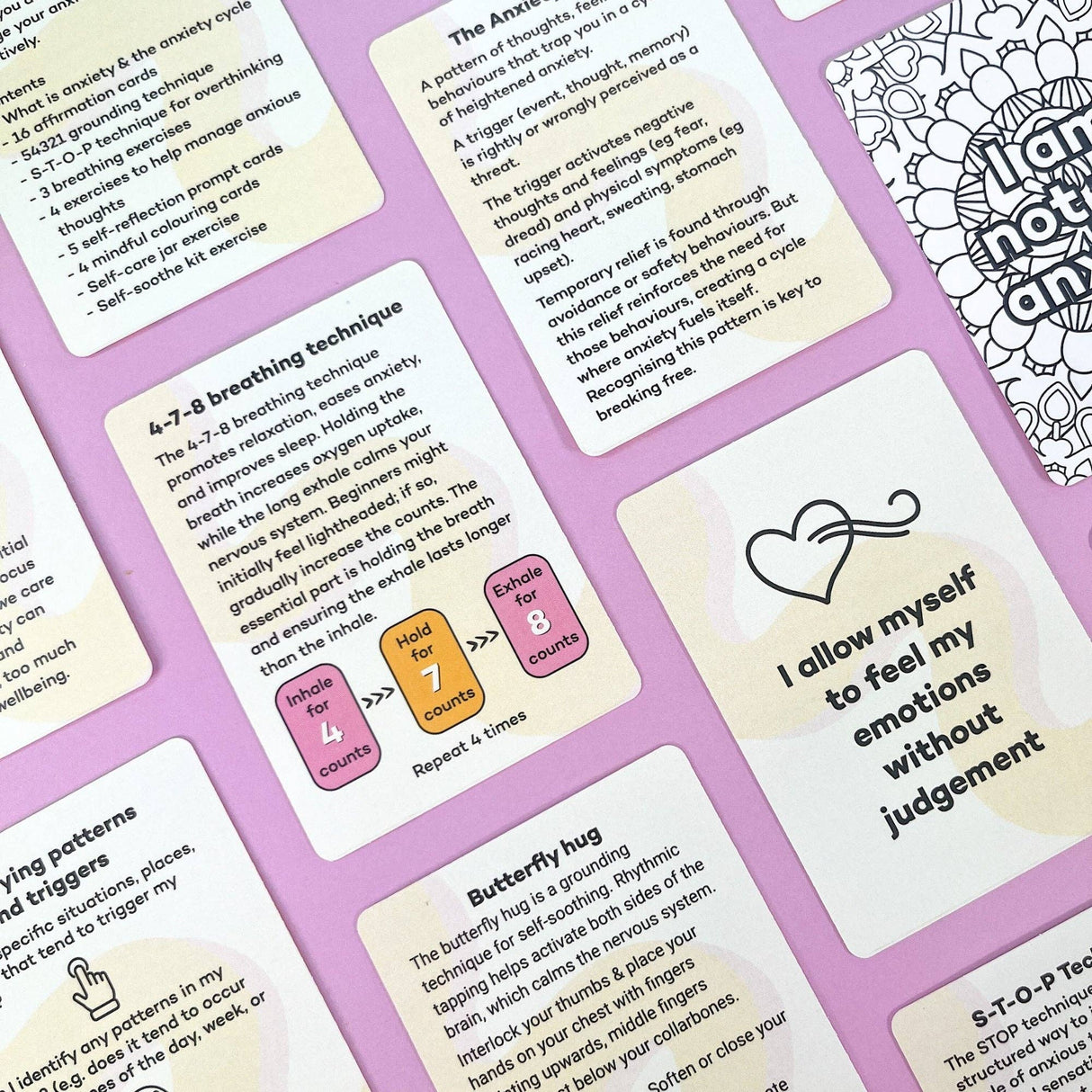 Flatlay of multiple Anxiety Toolkit cards showing content including the 4-7-8 breathing technique, affirmation cards, anxiety cycle explanation and butterfly hug grounding technique