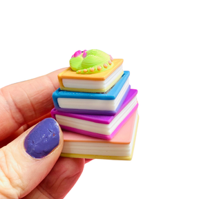Single sleeping dragon book stack clicker keychain held between fingers showing detail and size, on a white background