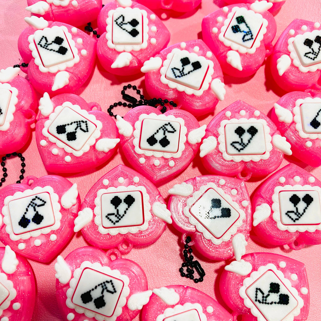 Flat lay of multiple pink heart clicker fidget keychains on a pink background showing varied pixel art designs