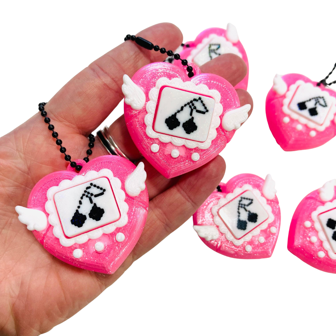 Pink heart-shaped keychains with black and white designs held in a hand, with additional keychains in the background.