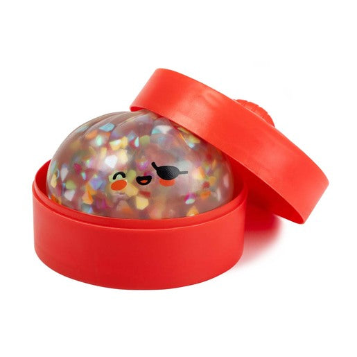 A red circular plastic container with a matching lid, shown open with a clear dome-shaped insert filled with multicolored glitter and a cute cartoon face, on a white background.
