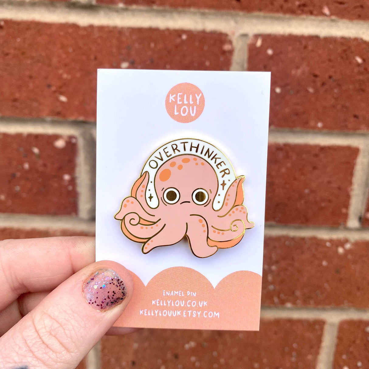 Pin with an octopus design on a card held against a brick wall