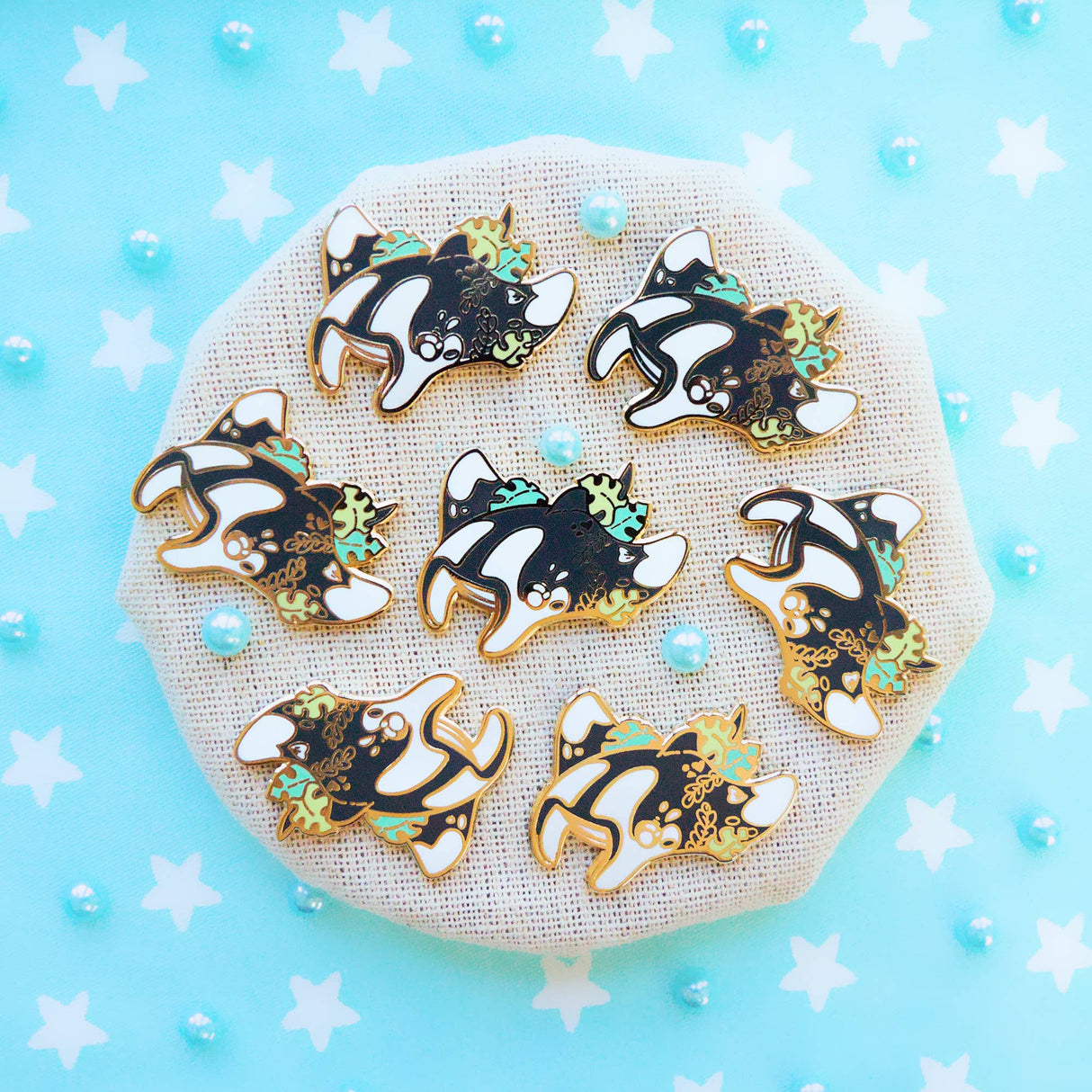 Evy Benita Oceanic Manta Ray enamel pins on round burlap display tray, blue background