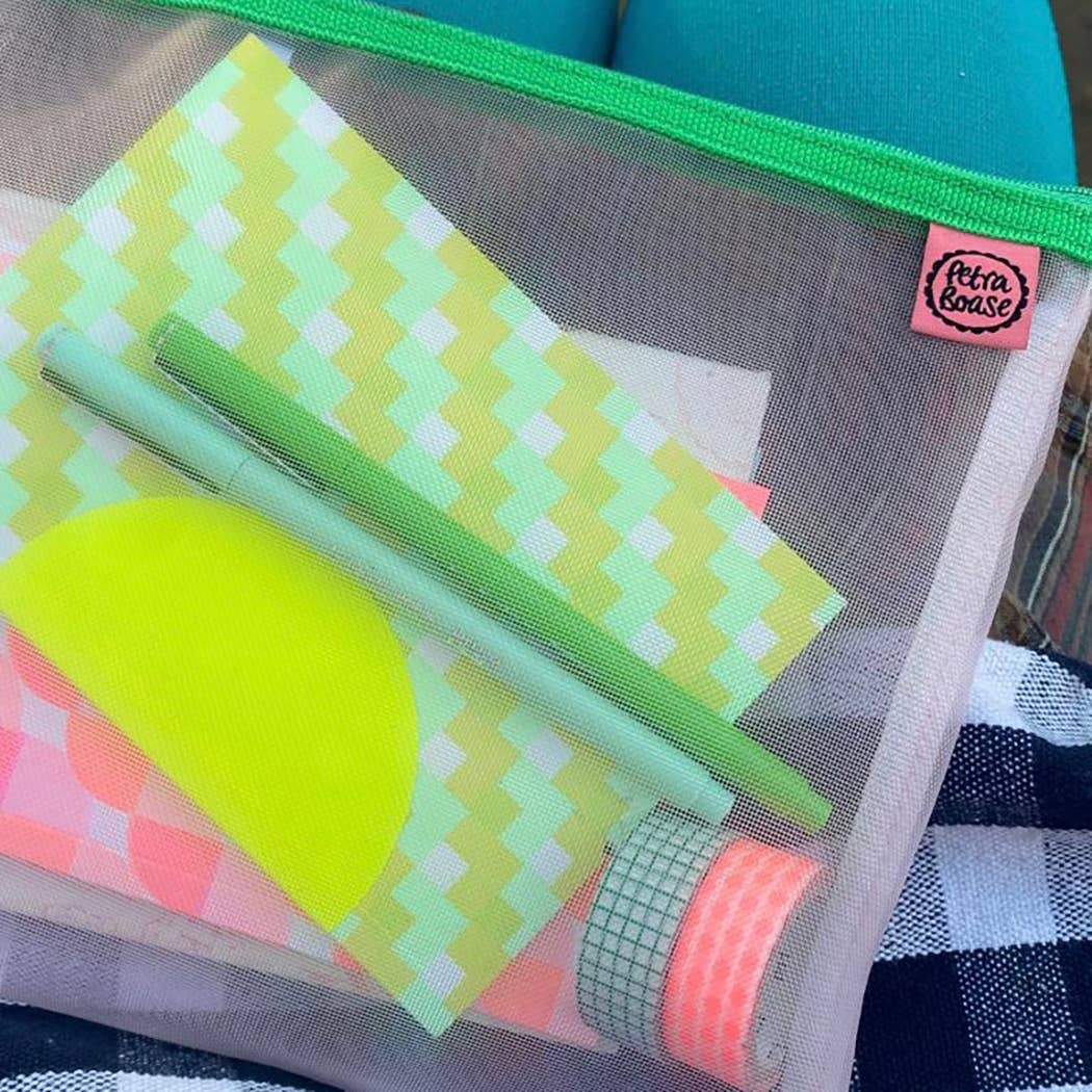 Mesh pouch with colorful items including a green pen, a notebook, and patterned paper.