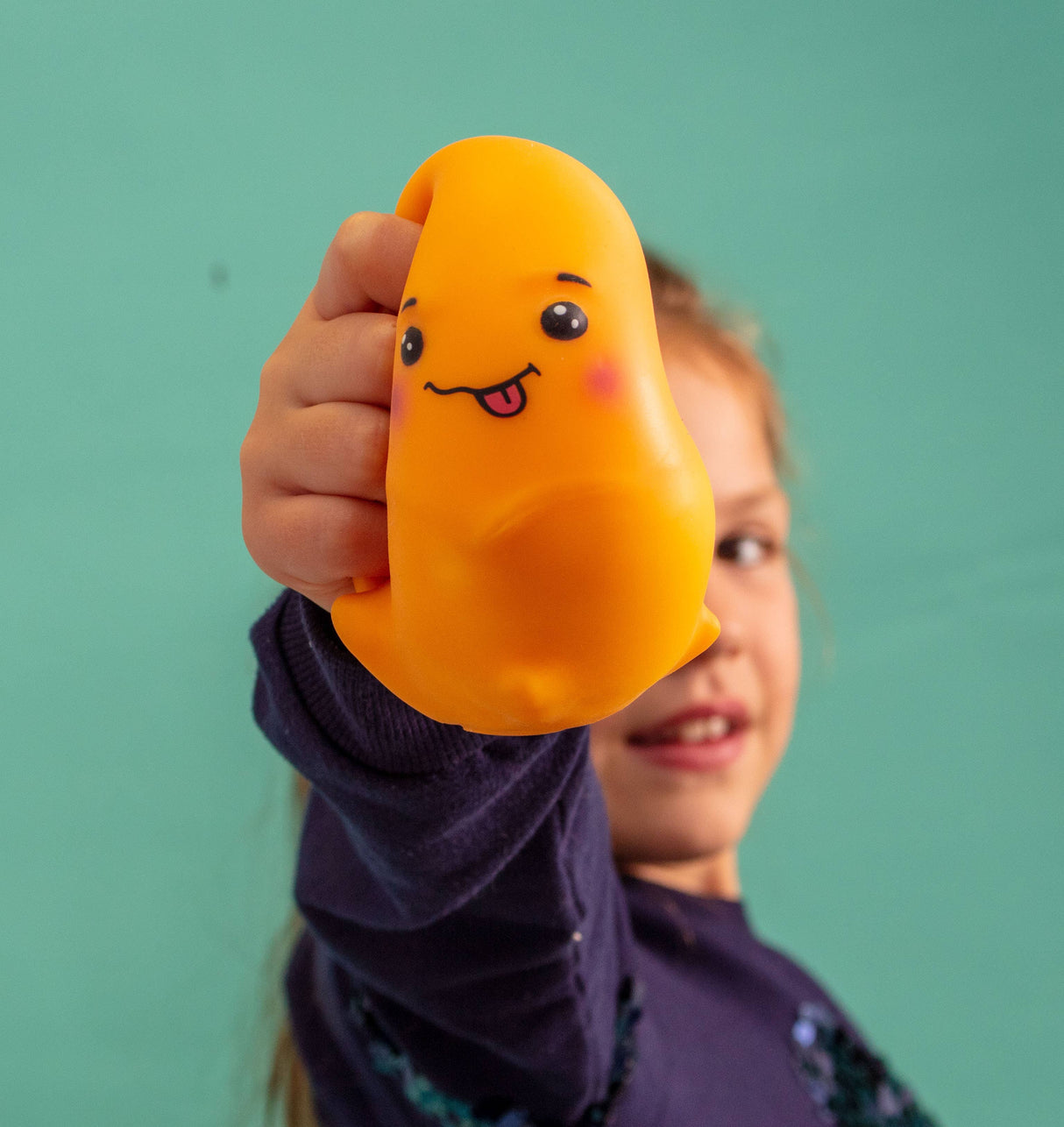 Hand holding the orange Jelly Squish kawaii jellyfish squishy against a teal background