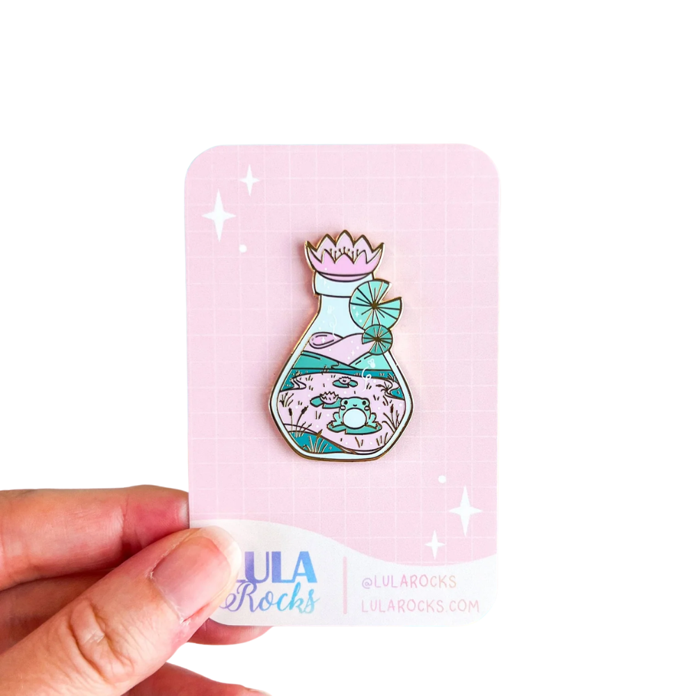 Lula Rocks Bottled Frog UV Glow enamel pin on pink backing card, white background