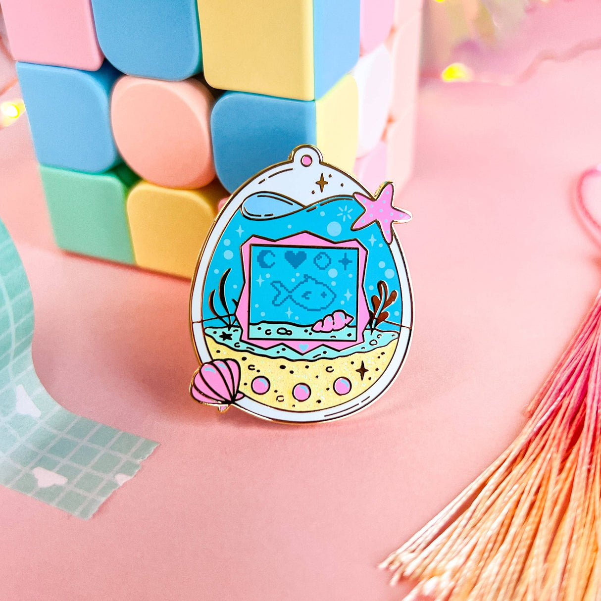 Lula Rocks Digital Aquarium enamel pin, blue pink, standing against pastel blocks