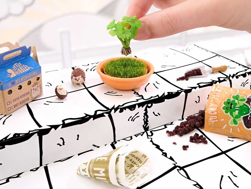 Hands building MGA Miniverse Make It Mini Animals hedgehog habitat scene with miniature soil plant and accessories