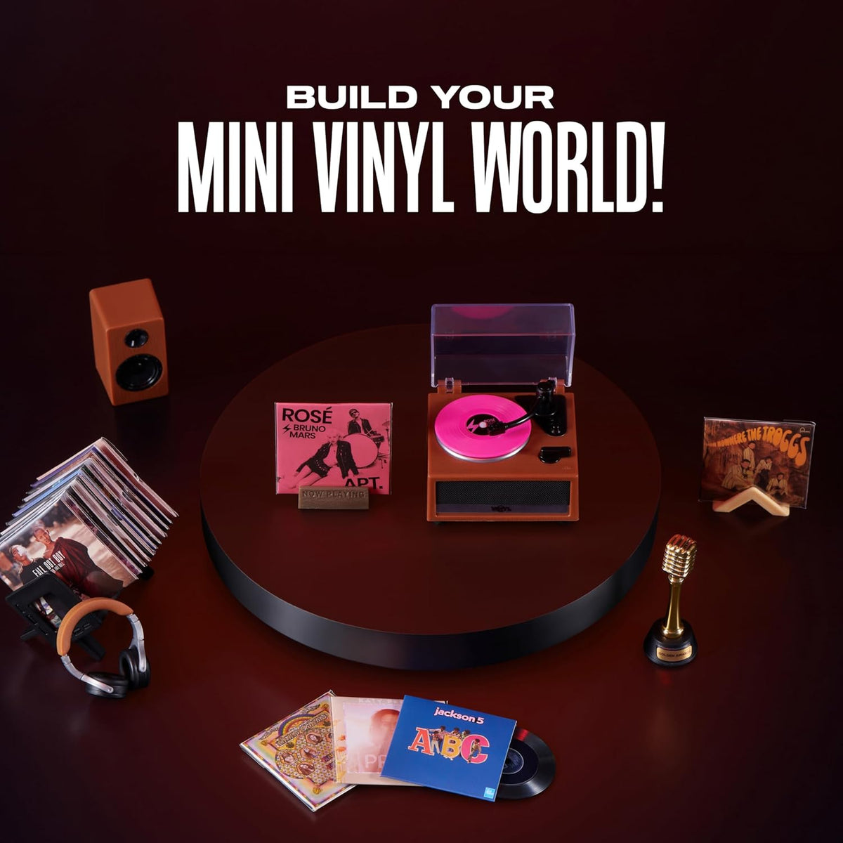 Mini record player with pink vinyl surrounded by miniature headphones, speaker and album sleeves