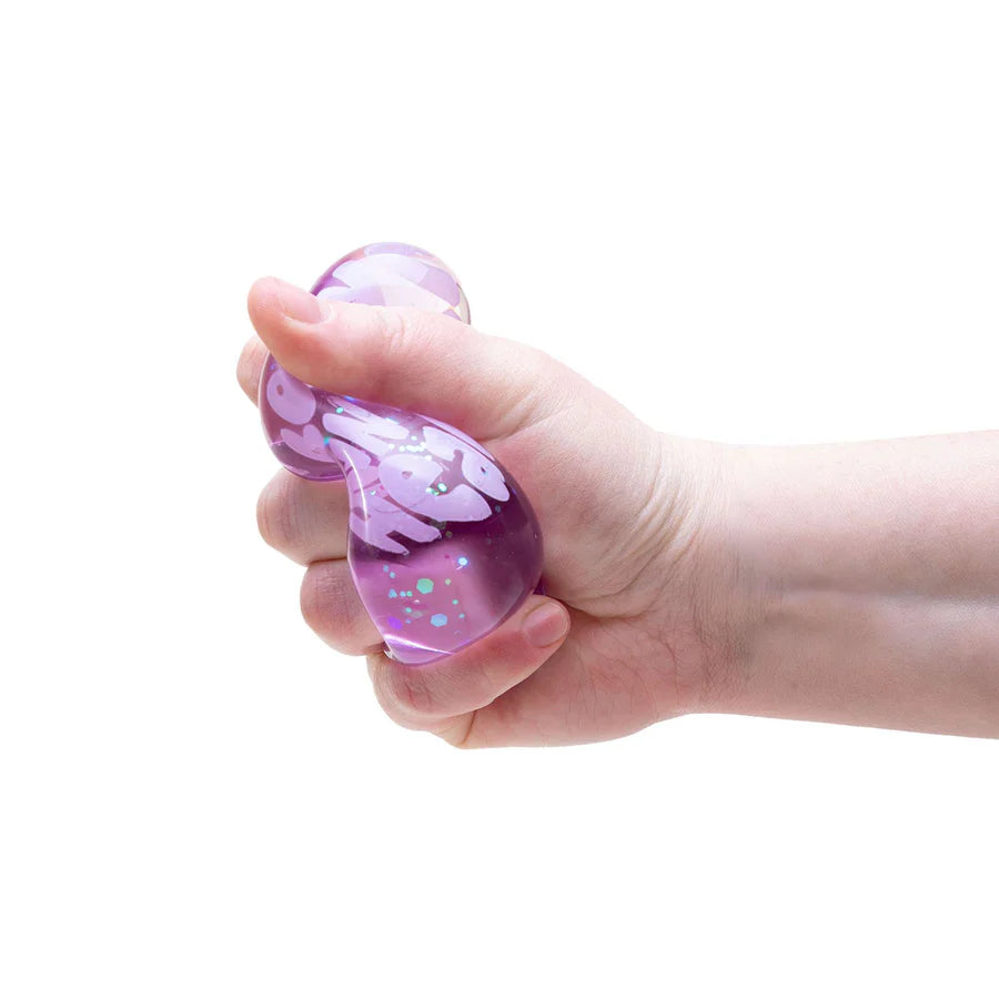 Hand squeezing a purple glitter Nee Doh Good Vibes Only heart showing satisfying squish deformation and glitter movement