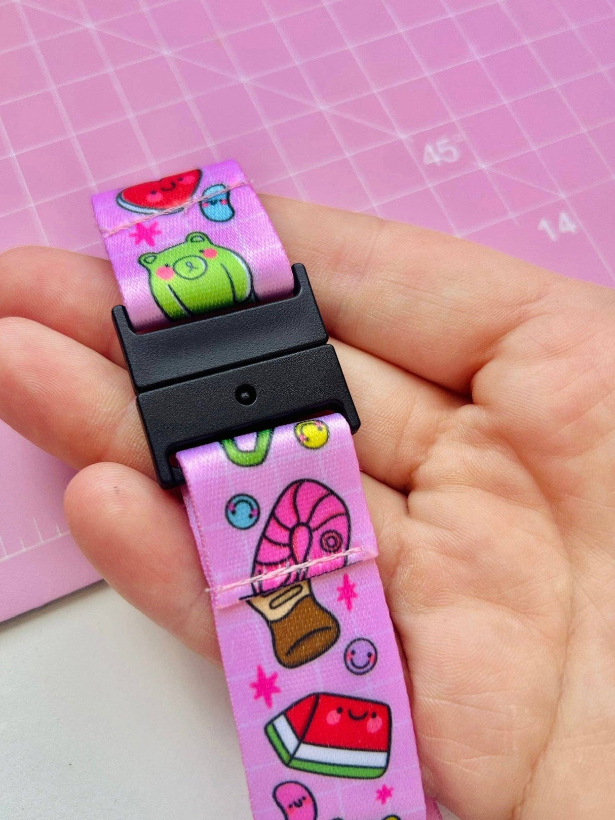 Close-up of the Pick 'n' Mix lanyard safety breakaway clasp held in an adult palm, showing kawaii frog and food print detail