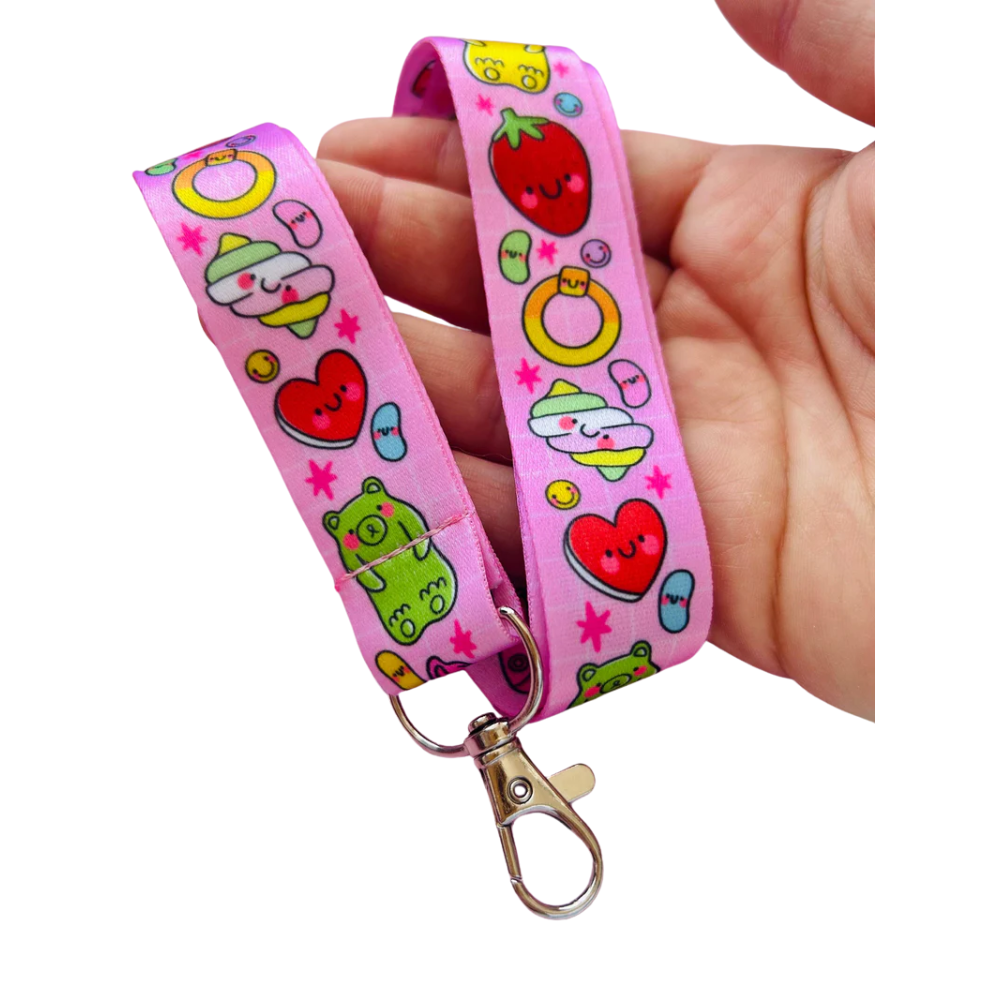 Adult hand holding the Pick 'n' Mix kawaii lanyard against a white background showing the full pink print with swivel clip