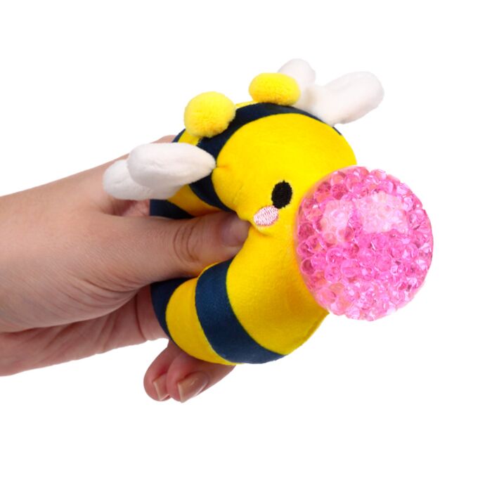 Hand squeezing a yellow striped plush bee Queasy Squeezie causing pink water bead nose to bulge out
