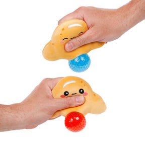 Two Queasy Squeezies croissant fidget plush toys squeezed in hands, blue and red
