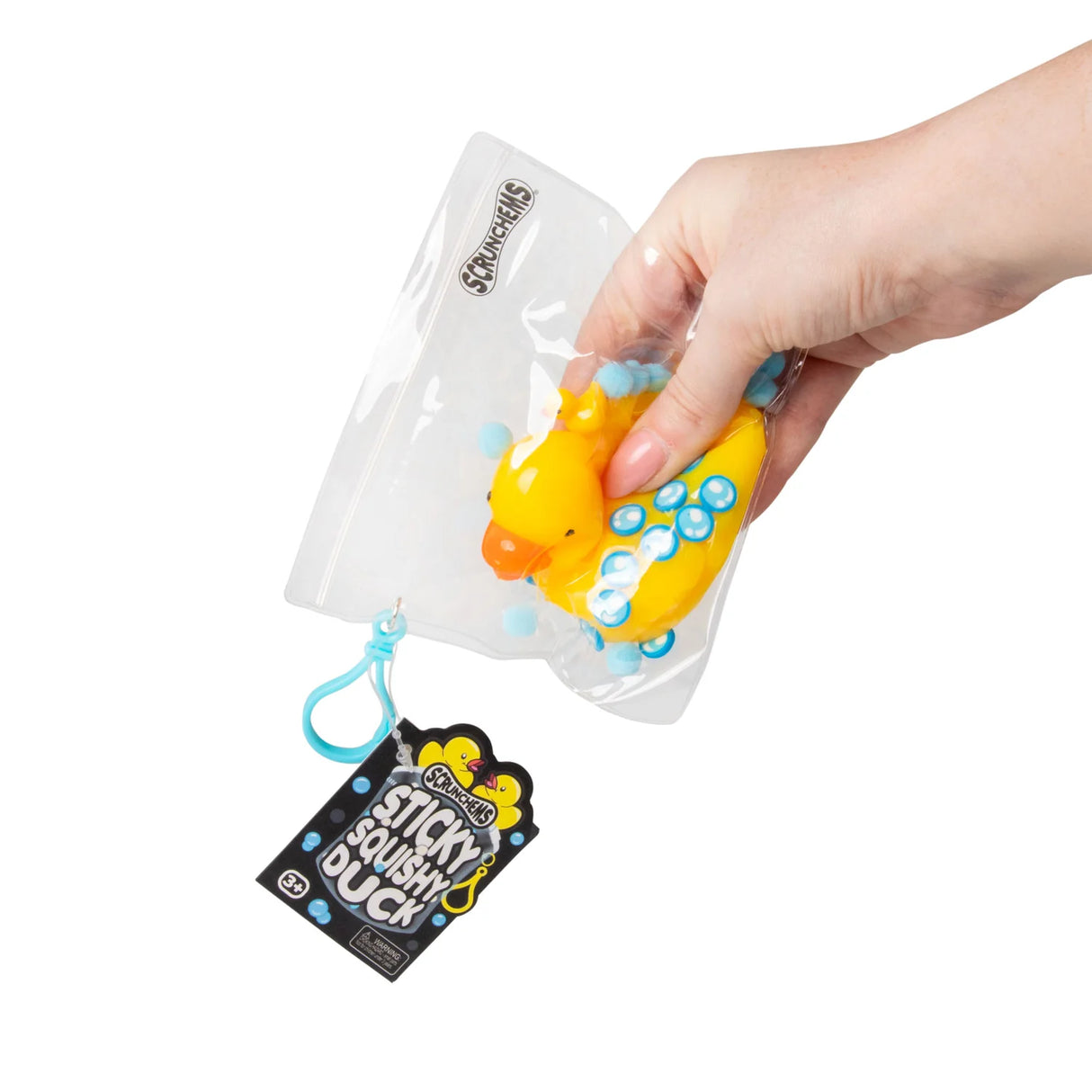 Hand squeezing a yellow Scrunchems Sticky Squishy Duck through its resealable packaging bag with teal clip hanger