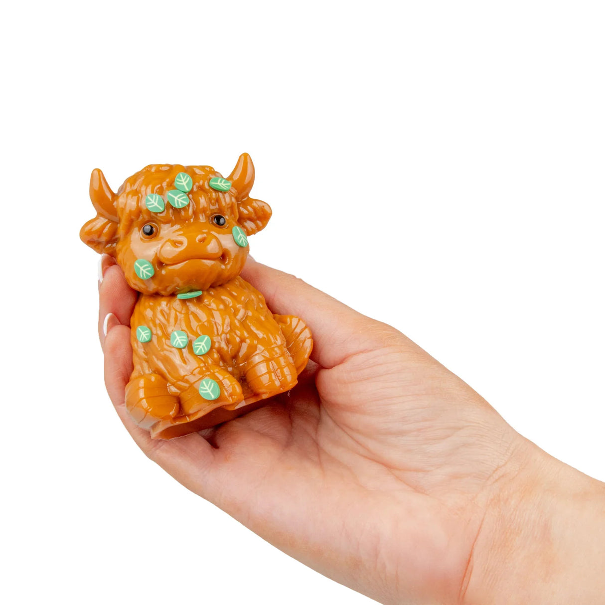 Golden-brown Scrunchems Highland Cow squishy toy with green leaf stickers resting on an open palm