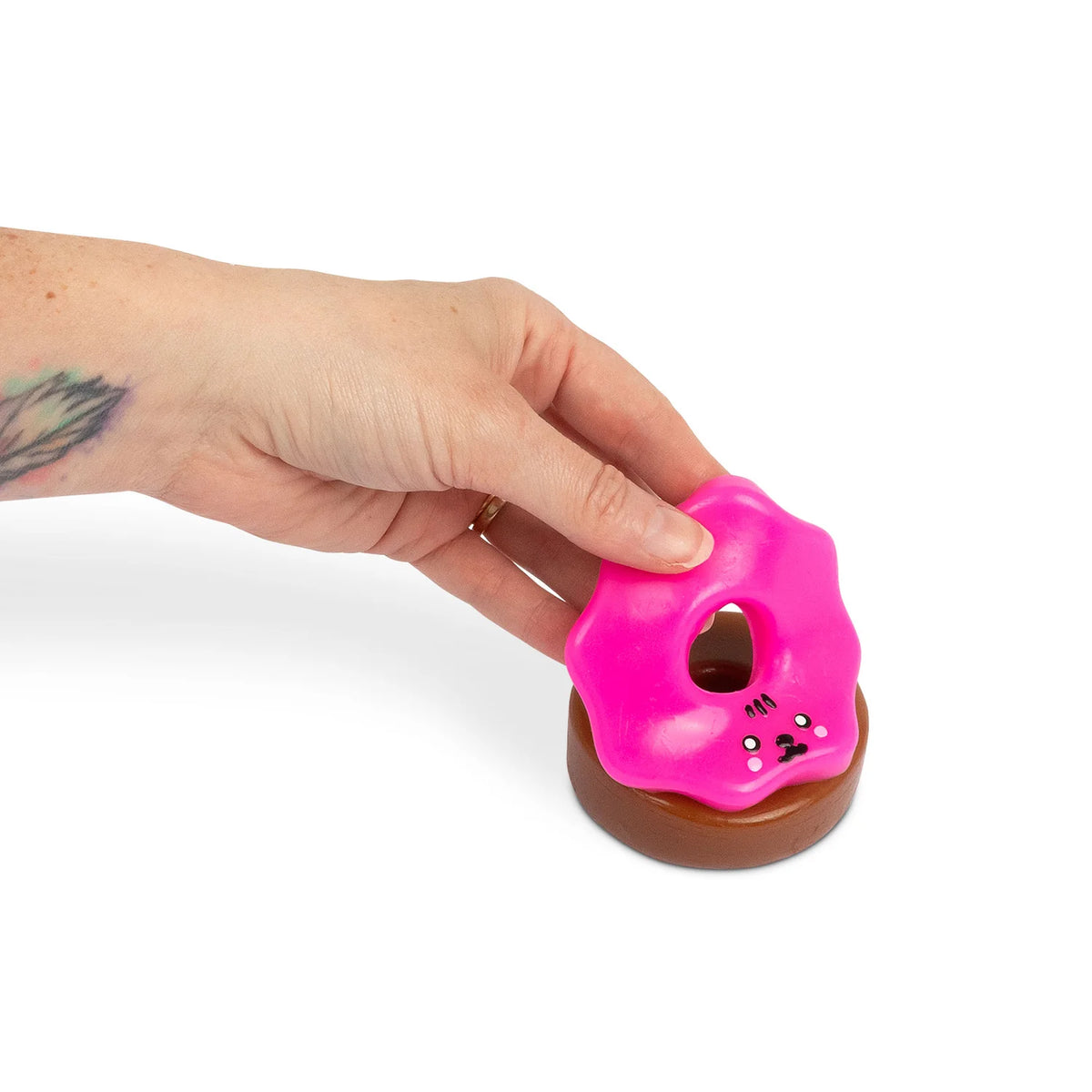 Hand placing hot pink sticky icing onto chocolate Scrunchems Sticky Squishy Donut base