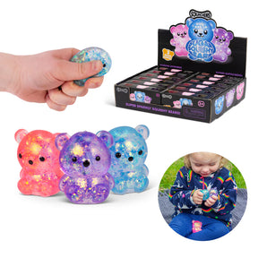 Three glitter Scrunchems Sugar Squishy Bears in pink, purple and blue shown with hand squeezing one and retail display box