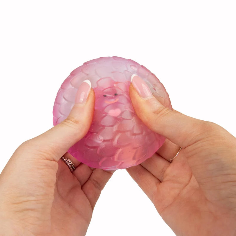 Hands squeezing pink Scrunchems Sugar Dragon Egg showing soft squishy dragon scale shell