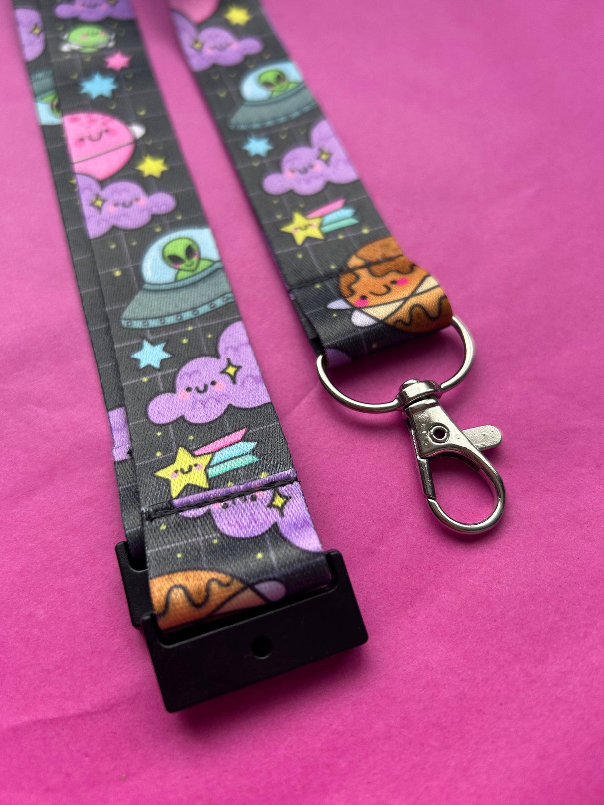 Close-up of the Space Cuties lanyard showing the metal swivel clip, key ring and safety breakaway clasp with space print detail