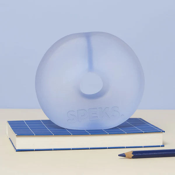 Periwinkle blue translucent Speks Gump Jumbo Loop standing upright on a desk beside a notebook