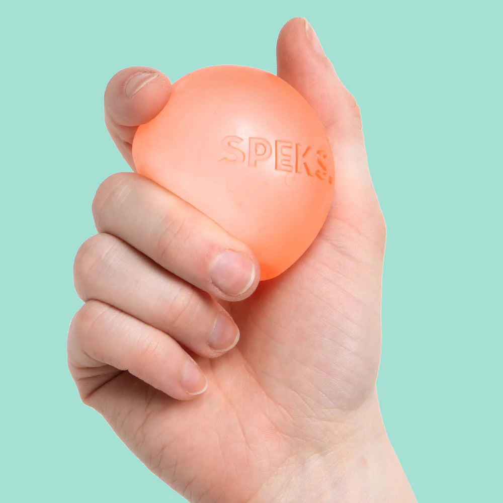 Hand holding a coral orange Speks Gump Original memory gel stress ball against a teal background