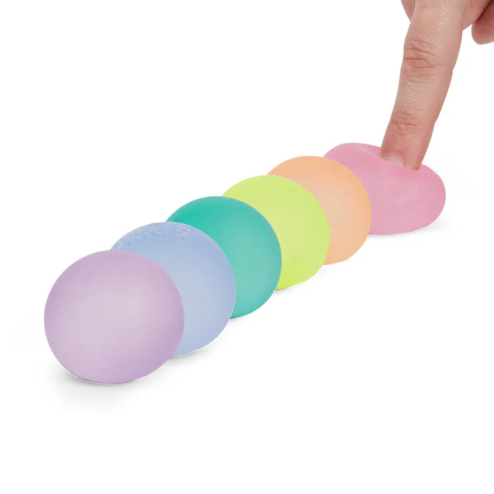 Six Speks Mini Gump memory gel stress balls lined up in a pastel rainbow row with a finger pressing down on the pink one