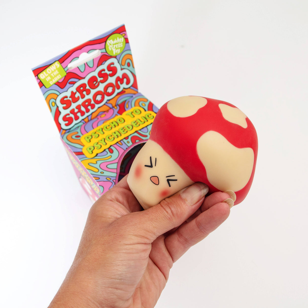 Hand squeezing the Stress Shroom mushroom squishy upside down with packaging behind