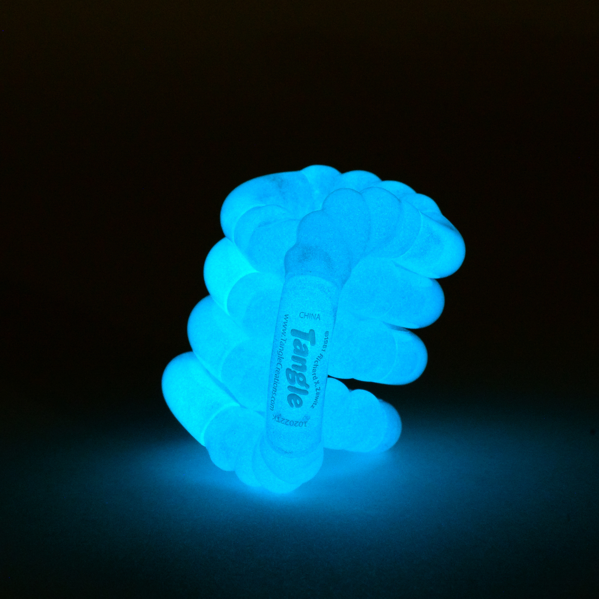 Orange glow-in-the-dark Tangle Jr. bumpy fidget toy glowing warm orange in the dark