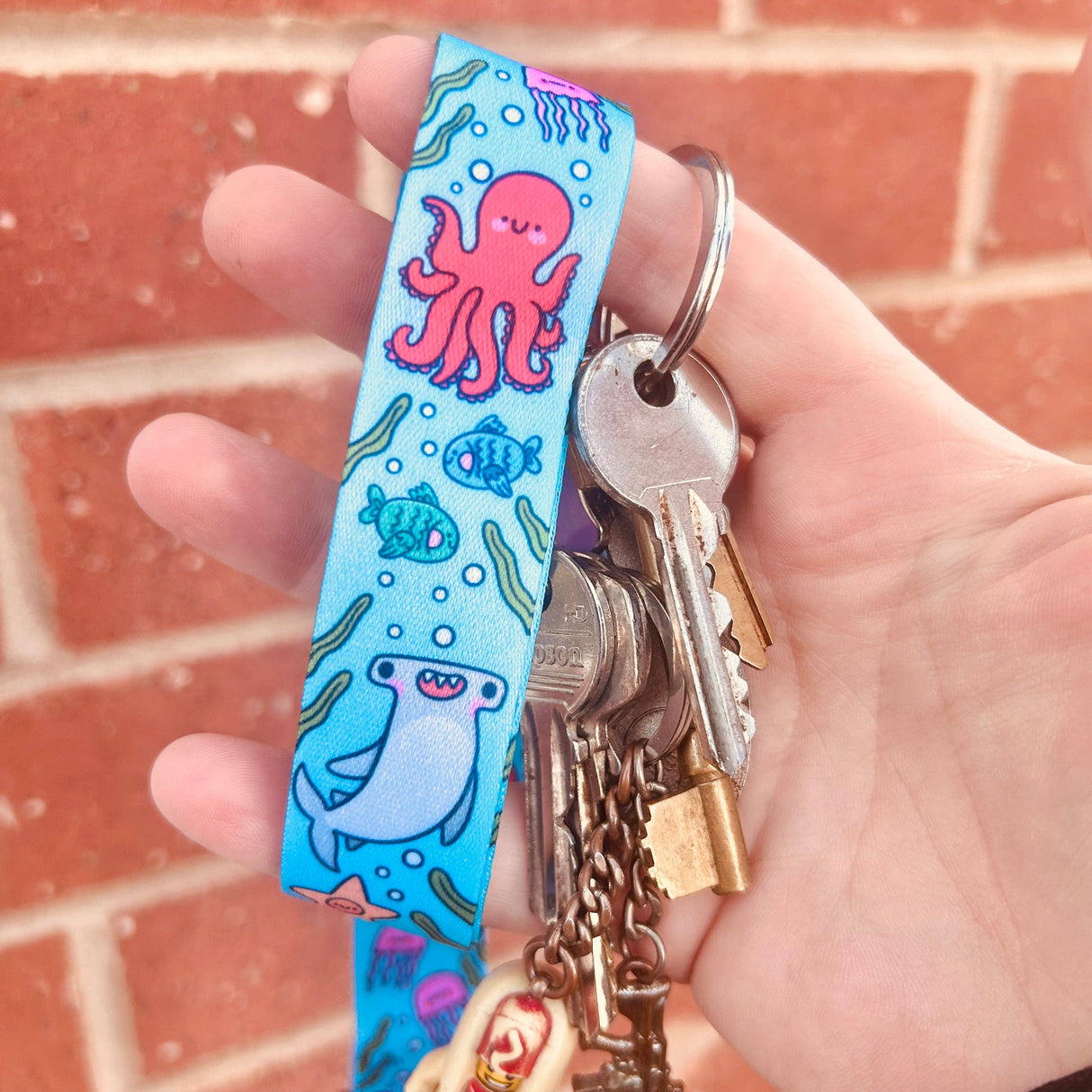Hand holding keys with a colorful keychain featuring marine life designs against a brick wall.