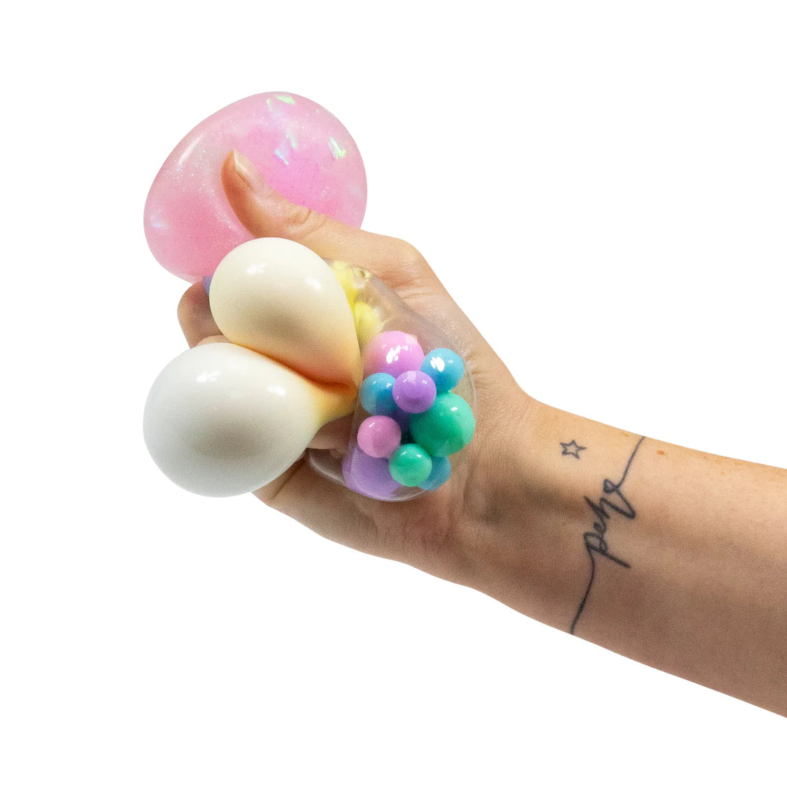 Adult hand squeezing all three unicorn squish ball varieties at once — pink glitter, white, and clear bead-filled