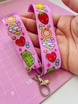 Adult hand holding the Pick 'n' Mix kawaii lanyard over a pink cutting mat showing the full print with gummy bears, strawberries and hearts