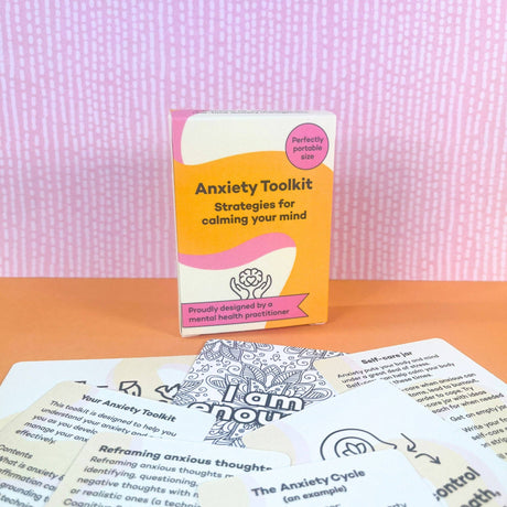 Anxiety Toolkit box displayed upright on an orange surface surrounded by fanned-out cards showing card content