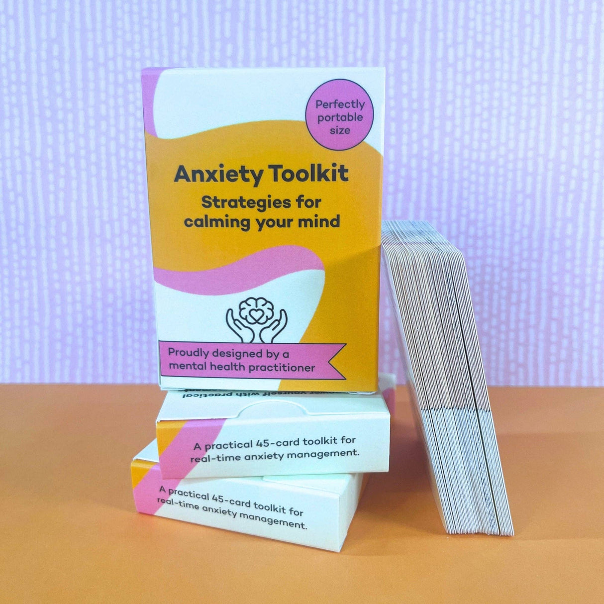 Three Anxiety Toolkit card deck boxes stacked with cards fanned out beside them on an orange surface