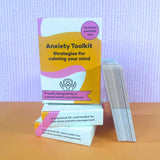 Three Anxiety Toolkit card deck boxes stacked with cards fanned out beside them on an orange surface