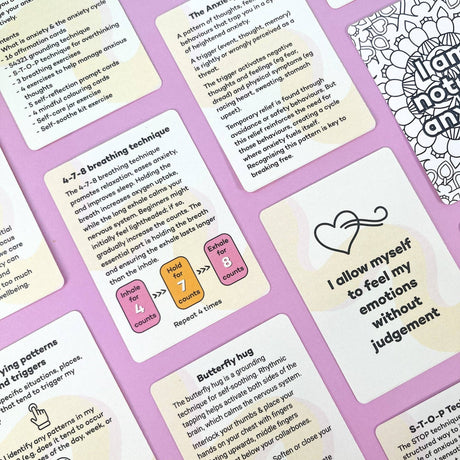 Flatlay of multiple Anxiety Toolkit cards showing content including the 4-7-8 breathing technique, affirmation cards, anxiety cycle explanation and butterfly hug grounding technique