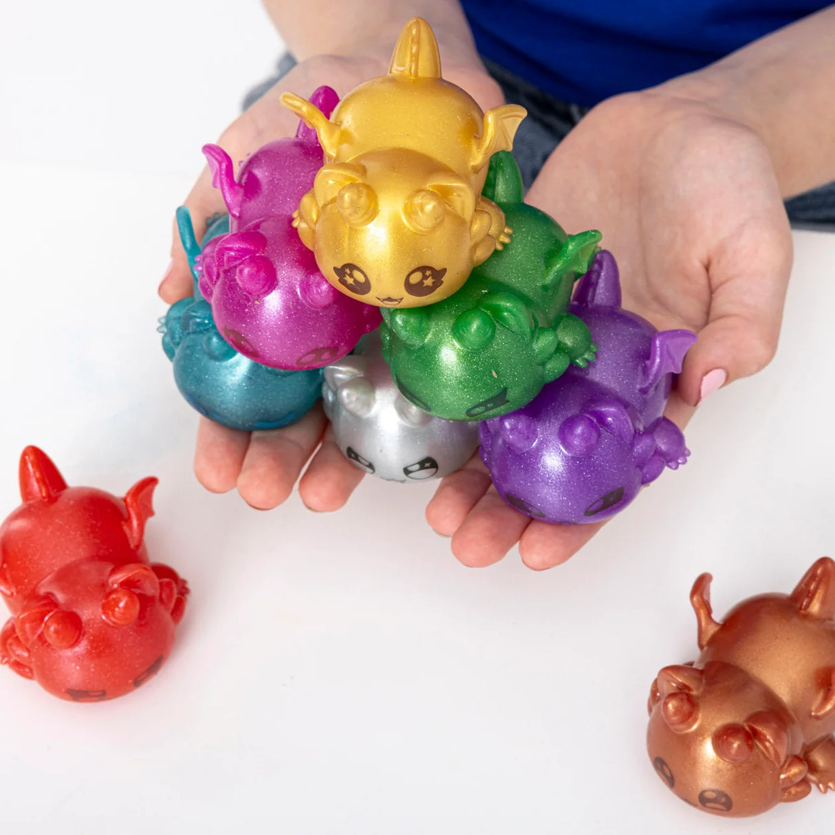 Hand holding a colourful pile of Aphmau MeeMeow squishy dragon figures in mixed shades