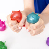 Two hands squeezing red and teal Aphmau MeeMeow squishy dragon fidget figures
