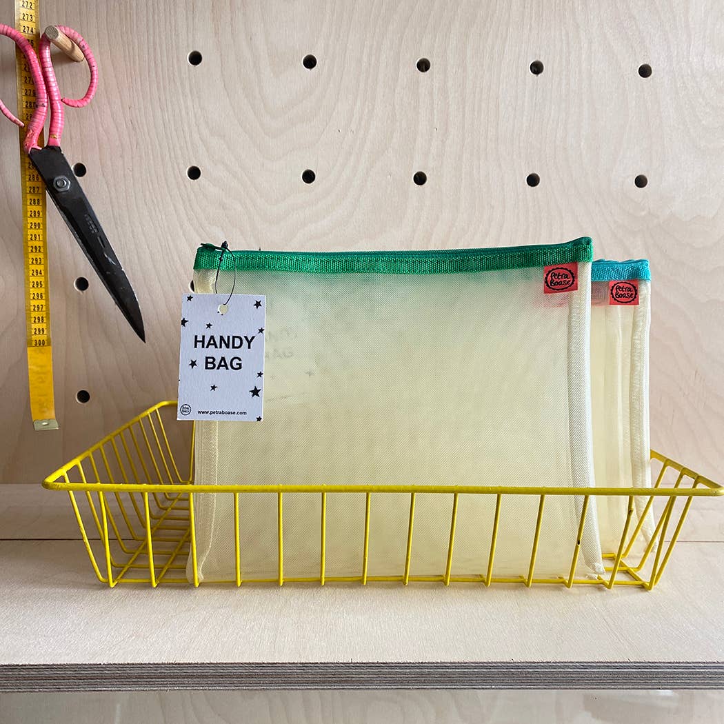 Yellow wire basket with a mesh bag labeled 'Handy Bag' on a wooden surface.