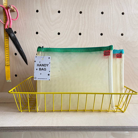 Yellow wire basket with a mesh bag labeled 'Handy Bag' on a wooden surface.