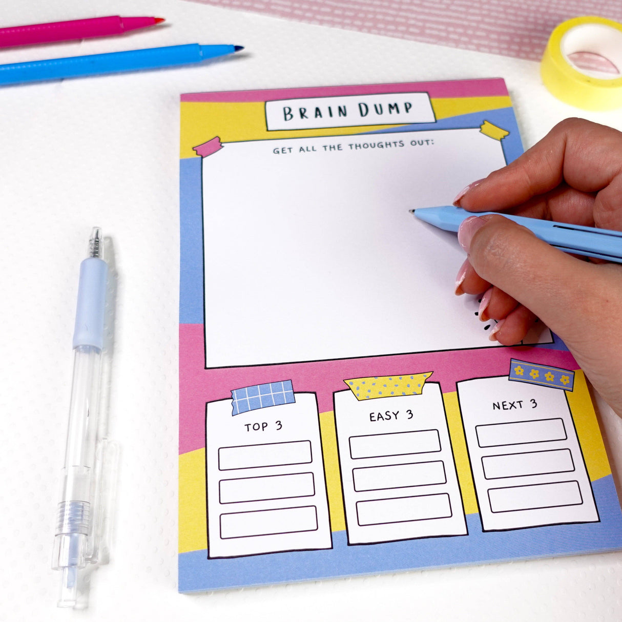 Colourful brain dump notepad with pink, blue and yellow design, being written in