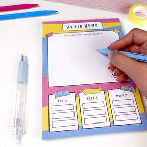 Colourful brain dump notepad with pink, blue and yellow design, being written in