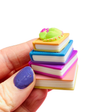 Single sleeping dragon book stack clicker keychain held between fingers showing detail and size, on a white background