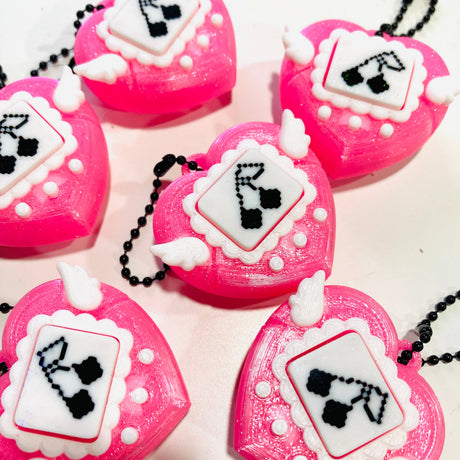 Close-up of multiple pink heart clicker fidget keychains showing pixel art screen detail and scalloped border