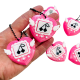 Pink heart-shaped keychains with black and white designs held in a hand, with additional keychains in the background.