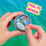 Hands peeling the label off a Crazy Aaron's Treasure Reveal Sneaky Snow putty tin