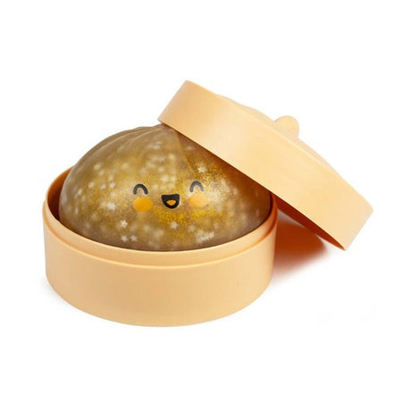 Golden glitter Crazy Fun Mystery Squishy Dumpling with a smiling face resting inside its peach steamer-style tub with the lid open